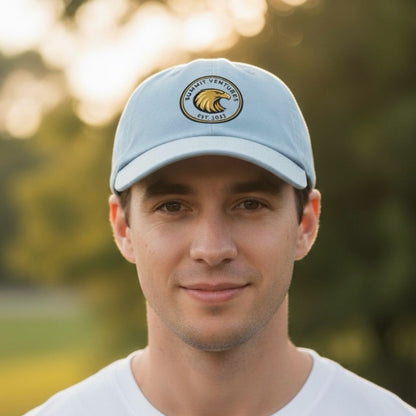Man wearing a light blue cap with a logo, outdoors with blurred greenery in the background