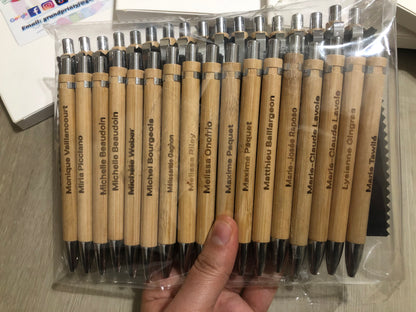 Packaged set of wooden pens with names engraved on them, held by a hand.